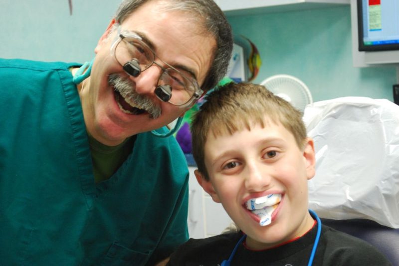 Dr. Joel Sokol wearing magnifying loupes and smiling next to a young patient wearing a fluoride tray.