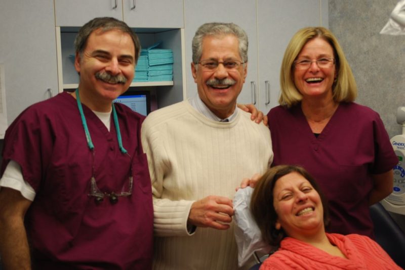 Dr. Joel Sokol alongside his practice team and a smiling couple of patients inside the treatment room.