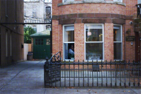 Exterior view of a brick building with large bay windows and a black wrought-iron fence, showing a view inside the office.