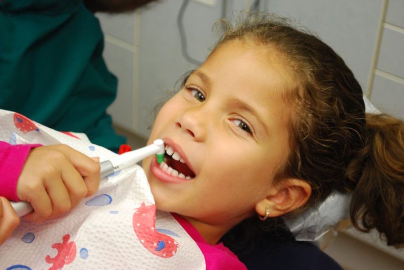 A young patient smiling in the dental chair while holding an electric toothbrush.